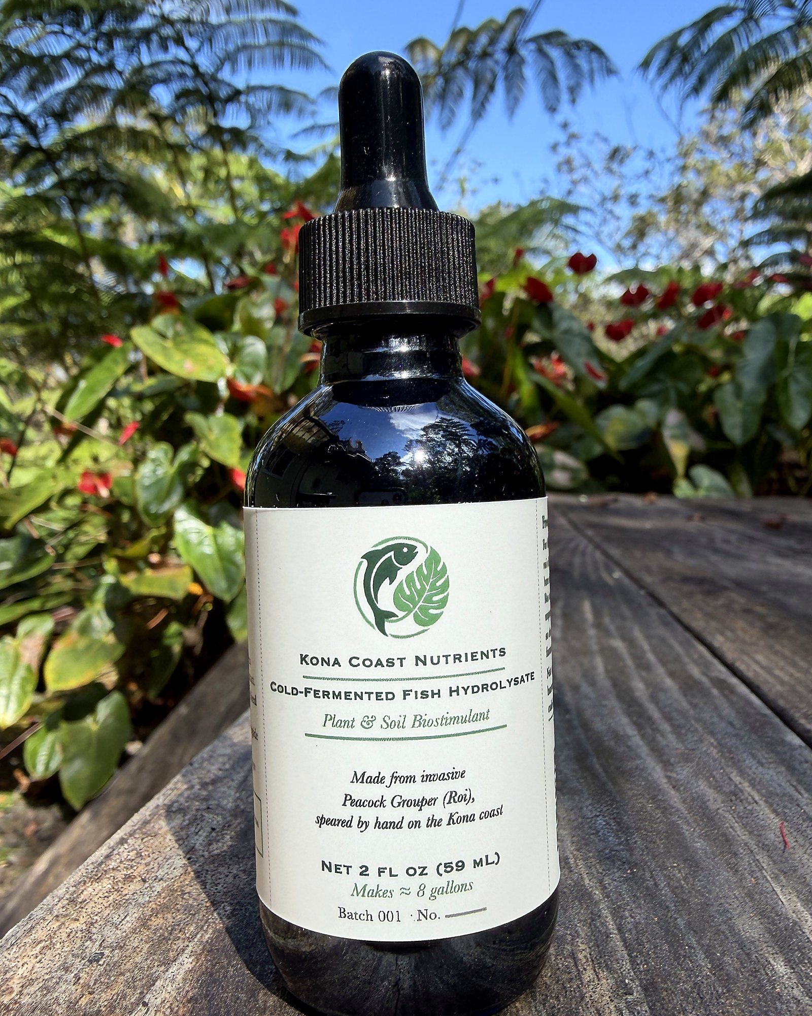 A 2 fl oz cobalt glass dropper bottle of Kona Coast Nutrients cold-fermented fish hydrolysate on a weathered wood table, Kona
